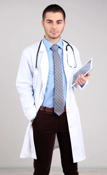 Doctor macho de pie con carpeta, sobre fondo gris —  Fotos de Stock