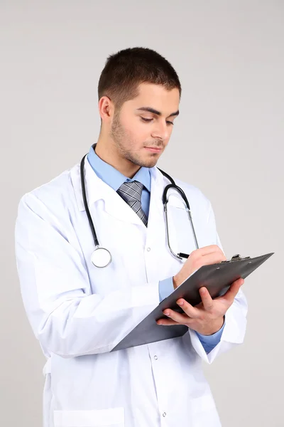 Male Doctor standing with folder, on gray background — Stock Photo, Image