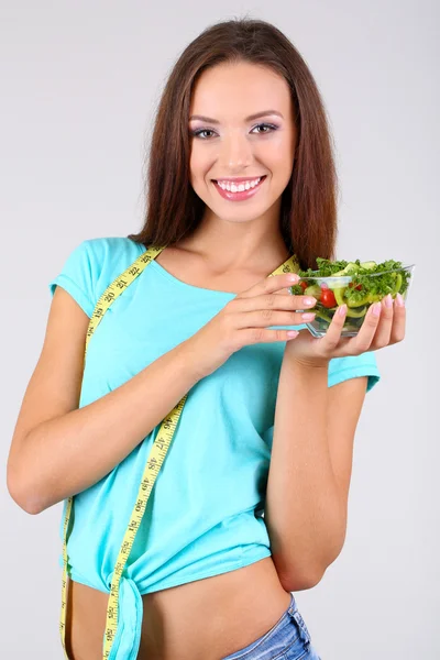 Beautiful girl with fresh salad on grey background — Stock Photo, Image