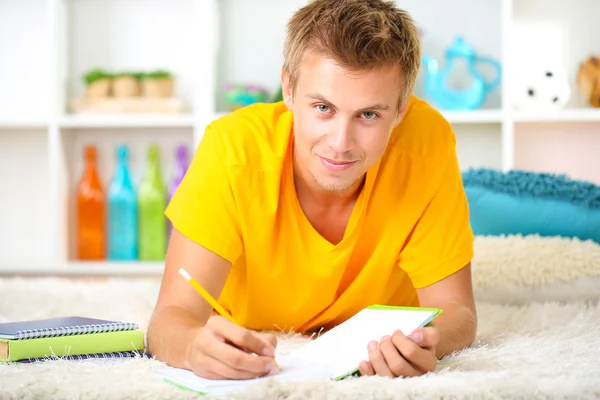 Junger Mann liegt auf Teppich und studiert, auf dem heimischen Interieur — Stockfoto