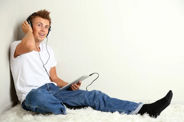 Junger Mann entspannt auf Teppich und hört Musik, auf grauem Wandhintergrund — Stockfoto