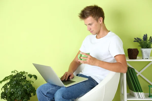 Ung man avkopplande med laptop i fåtölj, på hem inredning bakgrund — Stockfoto