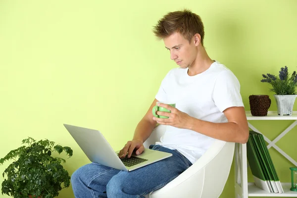 Hombre joven relajante con portátil en sillón, en el fondo interior de casa —  Fotos de Stock