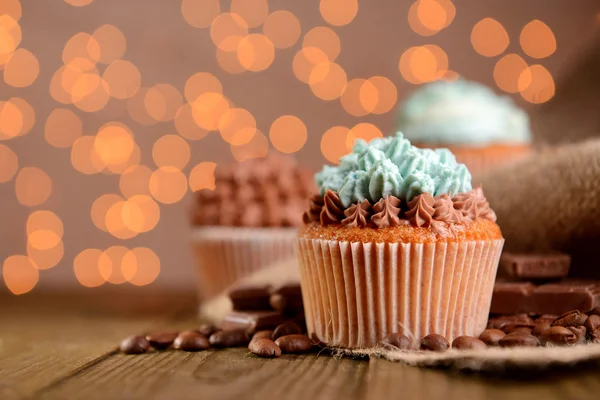 Sabrosos cupcakes con crema de mantequilla, sobre mesa de madera, sobre fondo de luces — Foto de Stock