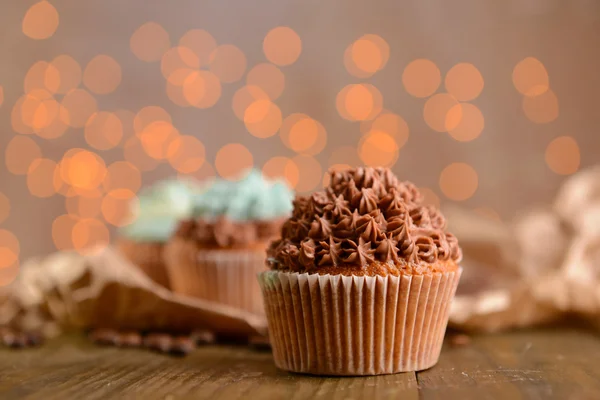 Sabrosos cupcakes con crema de mantequilla, sobre mesa de madera, sobre fondo de luces — Foto de Stock
