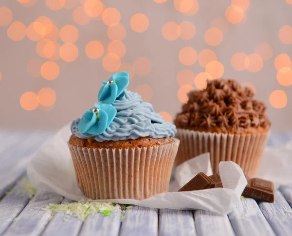 Sabrosos cupcakes con crema de mantequilla, sobre tabla de madera de color, sobre fondo de luces —  Fotos de Stock