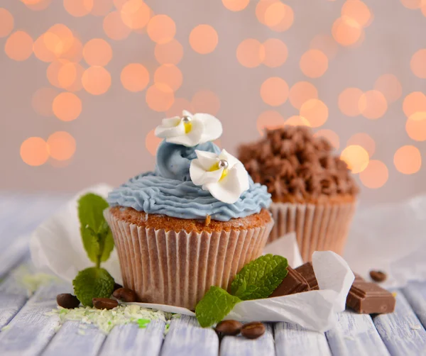 Sabrosos cupcakes con crema de mantequilla, sobre tabla de madera de color, sobre fondo de luces —  Fotos de Stock