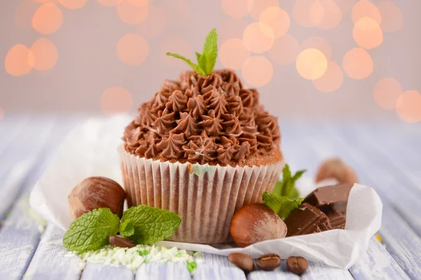 Sabroso cupcake con crema de mantequilla, sobre tabla de madera de color, sobre fondo de luces —  Fotos de Stock