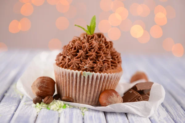 Sabroso cupcake con crema de mantequilla, sobre tabla de madera de color, sobre fondo de luces — Foto de Stock