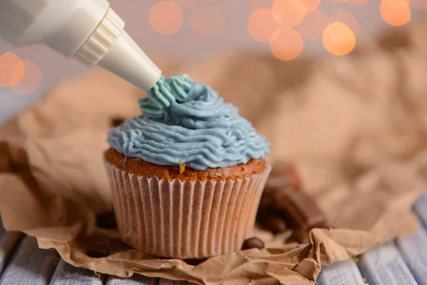 Confectioner decorating tasty cupcake with butter cream, on color wooden table, on lights background — Stock Photo, Image