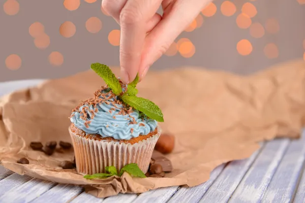 Kvinnlig hand dekorera läckra cupcake med smör grädde, på trä färgtabell på ljus bakgrund — Stockfoto