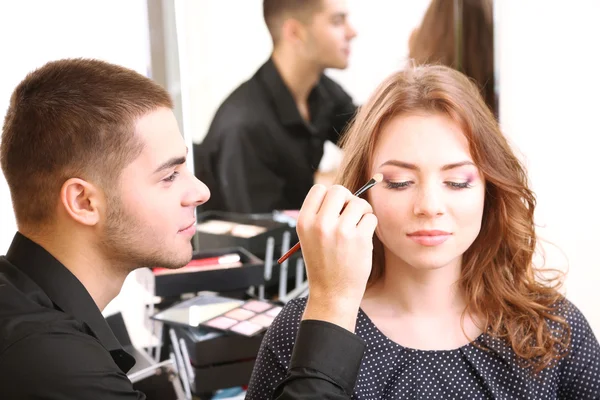 Young guy stylist doing makeup beautiful woman in beauty salon — Stock Photo, Image