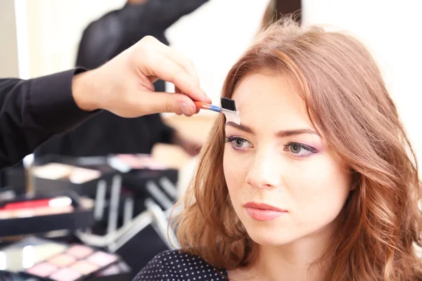 Joven estilista haciendo maquillaje hermosa mujer en salón de belleza — Foto de Stock