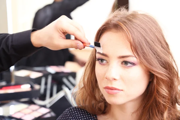 Joven estilista haciendo maquillaje hermosa mujer en salón de belleza —  Fotos de Stock