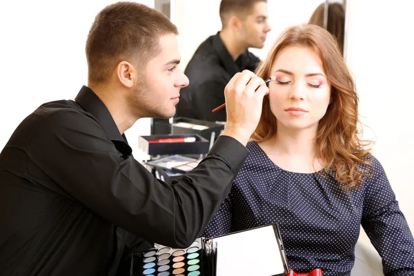 Young guy stylist doing makeup beautiful woman in beauty salon — Stock Photo, Image