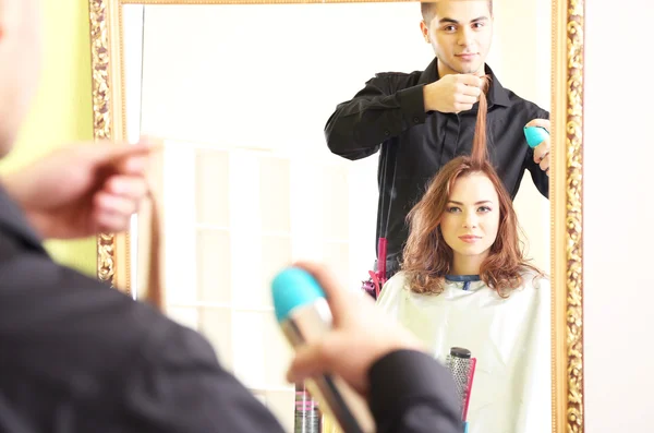 Молодой человек парикмахер делает прическу девушке в салоне красоты — стоковое фото