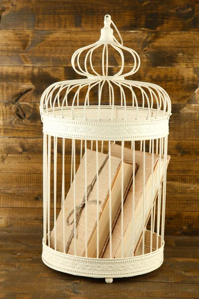 Books in decorative cage on wooden background — Stock Photo, Image