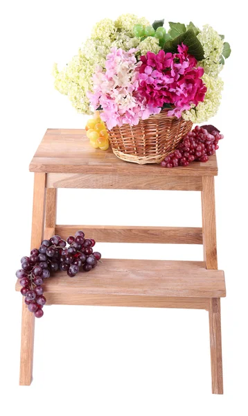 Wicker basket with flowers and fruits, on small wooden ladder, isolated on white — Stock Photo, Image