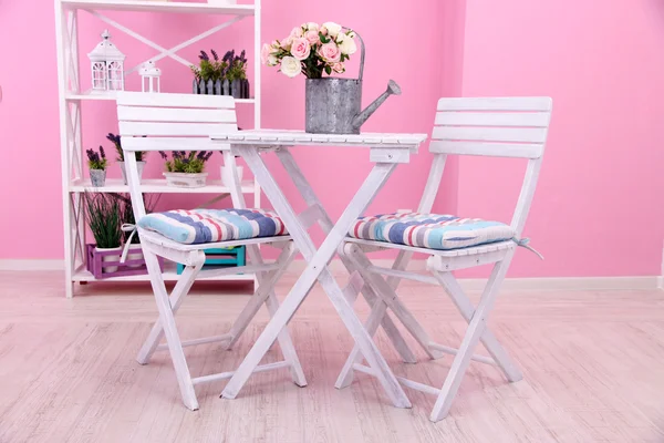 Garden chairs and table with flowers on shelves on pink background — Stock Photo, Image