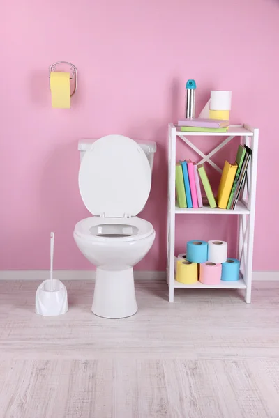 Tazón de inodoro blanco y soporte con libros, sobre fondo de pared de color — Foto de Stock