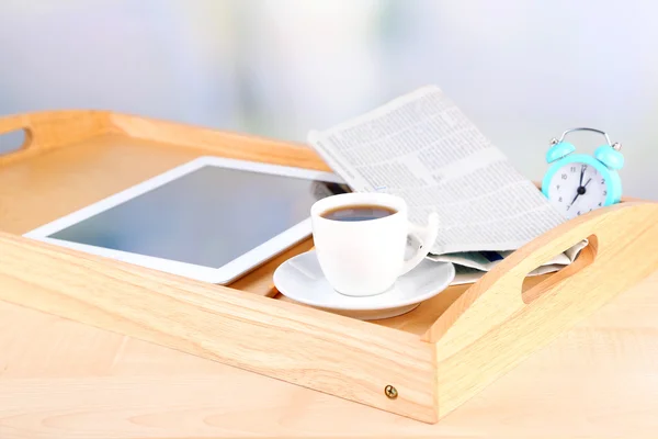 Tablet, newspaper, cup of coffee and alarm clock on wooden tray — Stock Photo, Image