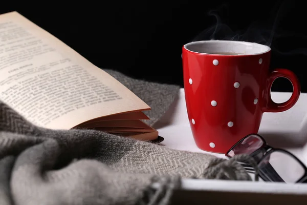 Чашка горячего чая с книгой и клеткой на столе на темном фоне — стоковое фото