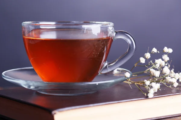 Tasse de thé chaud sur le livre avec des fleurs sur la table sur fond gris — Photo