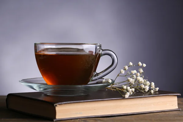 灰色の背景上のテーブルの上に花と本で熱いお茶のカップ — ストック写真