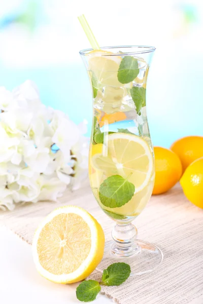 Glass of cocktail with lemon and mint on table on light blue background — Stock Photo, Image