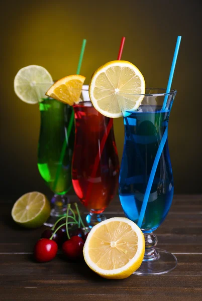 Glasses of cocktails on table on dark yellow background — Stock Photo, Image