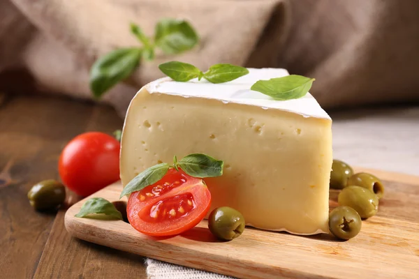 Tasty Camembert cheese with tomatoes, olives and basil, on wooden table — Stock Photo, Image