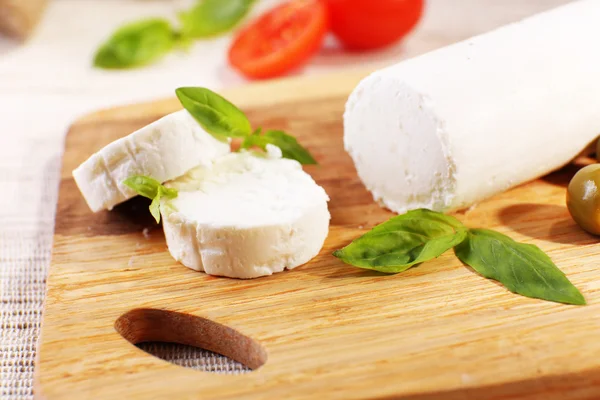 Вкусный сыр буше с помидорами, оливками и базиликом, на разделочной доске — стоковое фото