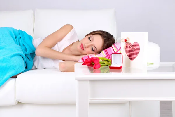 Όμορφη νεαρή γυναίκα που κοιμάται στον καναπέ κοντά σε πίνακα με δώρα και λουλούδια, κοντινό πλάνο — Φωτογραφία Αρχείου
