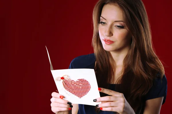 Aantrekkelijke vrouw met briefkaart, op rode achtergrond — Stockfoto