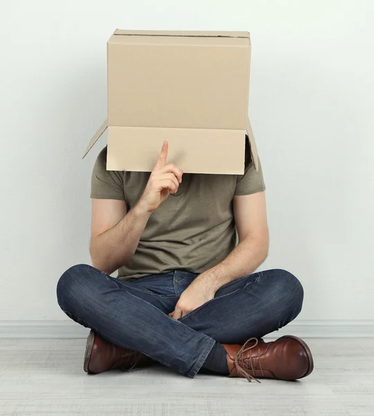Homem com caixa de papelão na cabeça sentado no chão perto da parede — Fotografia de Stock