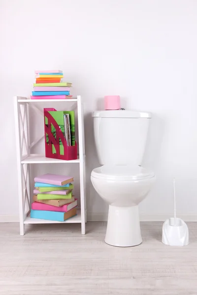 Tazón de inodoro blanco y soporte con libros, sobre fondo de pared de color — Foto de Stock