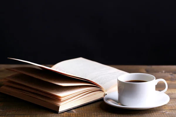 Kop warme koffie met boek op tafel op donkere achtergrond — Stockfoto