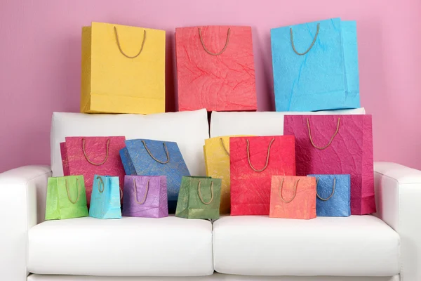 Colorful shopping bags on sofa, on color wall background — Stock Photo, Image