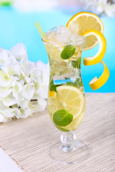 Bicchiere di cocktail con limone e menta sul tavolo su sfondo azzurro — Foto Stock