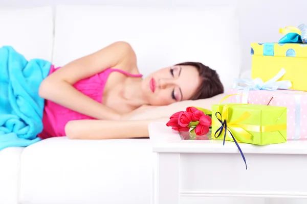 Hermosa joven que duerme en el sofá cerca de la mesa con regalos y flores, de cerca —  Fotos de Stock