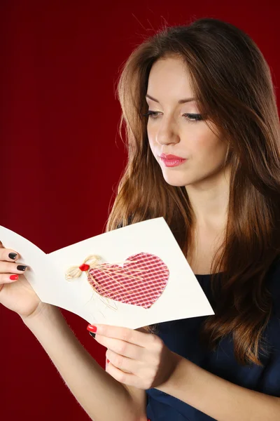 Attraktive Frau mit Postkarte, auf rotem Hintergrund — Stockfoto