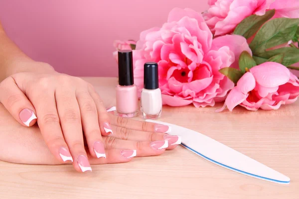 Hermosas manos de mujer con manicura francesa y flores en la mesa sobre fondo rosa — Foto de Stock