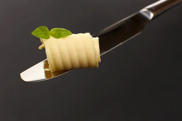 Curl of fresh butter with basil on knife on grey background — Stock Photo, Image