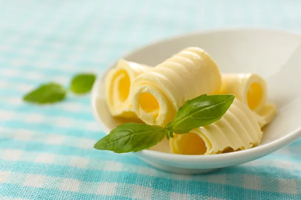 Curls of fresh butter with basil in bowl, on blue tablecloth