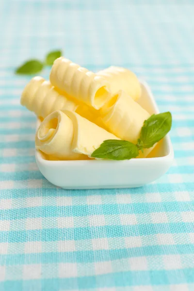 Curls of fresh butter with basil in bowl, on blue tablecloth — Stock Photo, Image