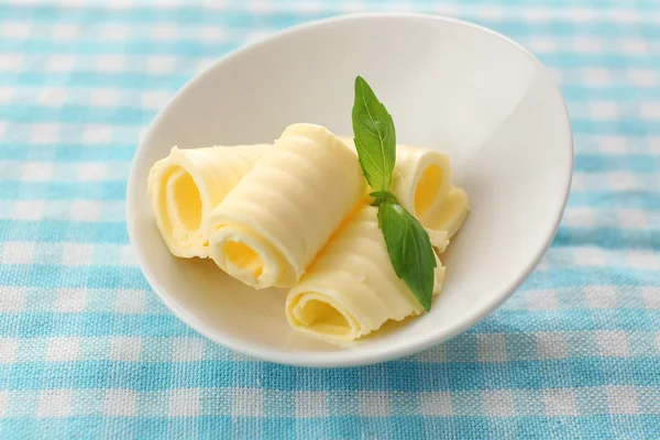 Curls of fresh butter with basil in bowl, on blue tablecloth — Stock Photo, Image