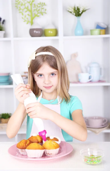 Pieni tyttö koristelu cupcakes keittiössä kotona — kuvapankkivalokuva