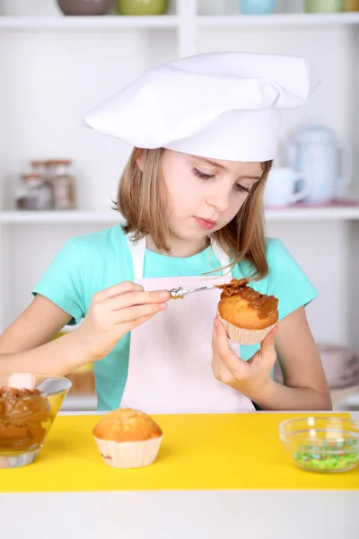 Little girl decorating cupcakes in kitchen at home — Stock Photo, Image