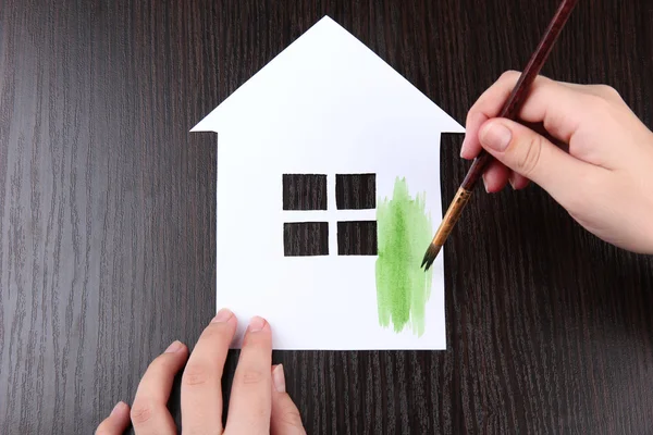 Female hand coloring paper cabin, on wooden background — Stock Photo, Image