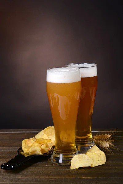 Vasos de cerveza con merienda en la mesa sobre fondo oscuro —  Fotos de Stock